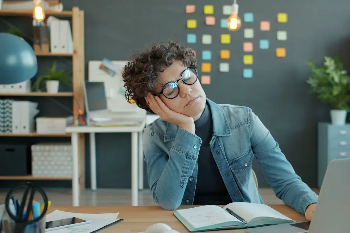 An exhausted office worker resting their head on one hand at a desk